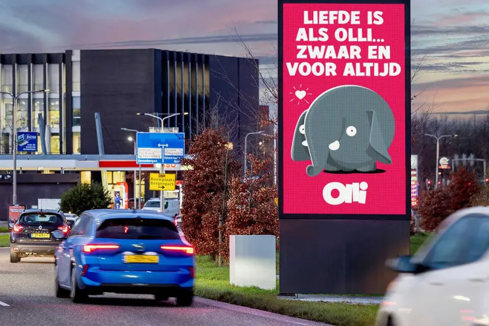Een digitaal reclamescherm van Centercom langs een doorgaande weg, met verkeer ervoor