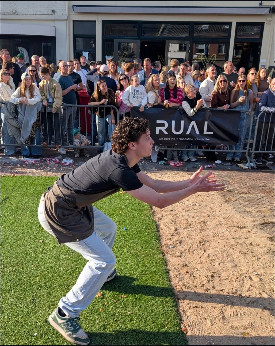 A competitor catching an egg at the Princenhage egg-throwing championship, in front of a RUAL banner and the crowd behind the barriers.